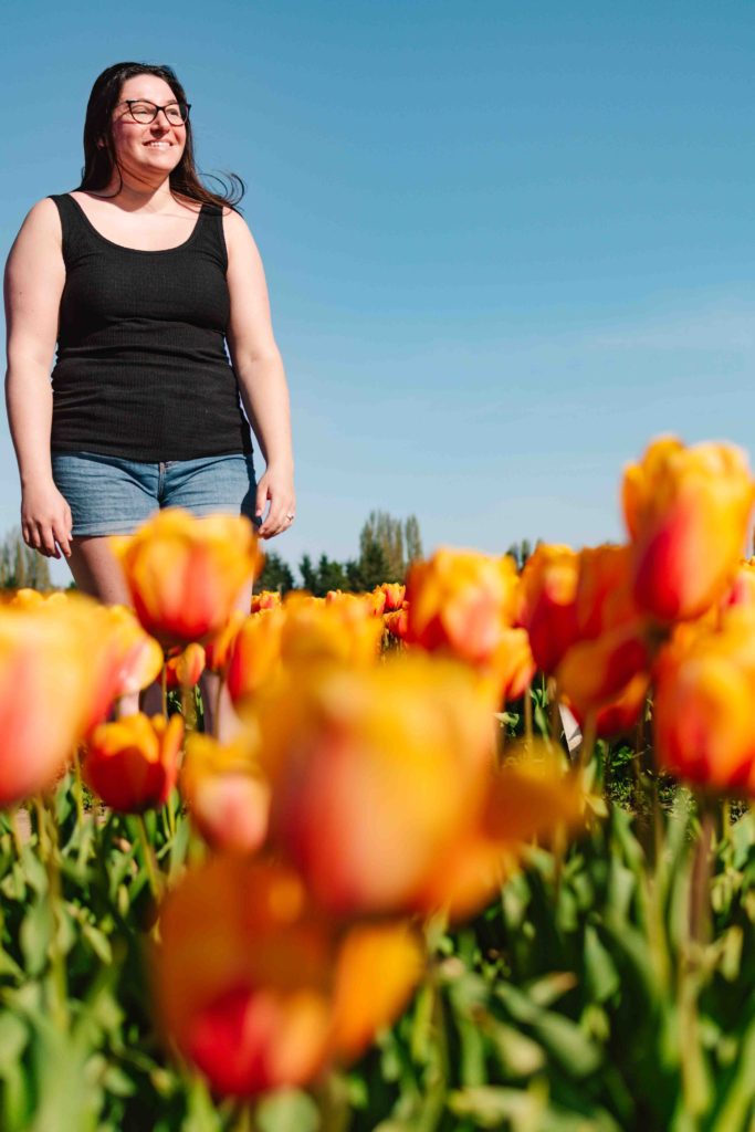 woman standing in a tulip farm safely with orange and red tulips in front