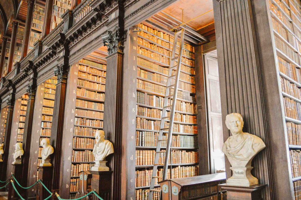 two story library with stacks of old books and busts and a rolling ladder