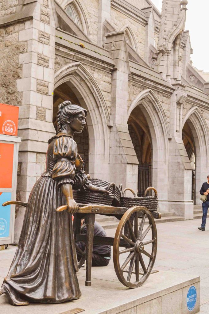 statue of a woman with a cart of baskets made of brass with arches behind