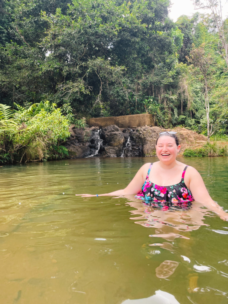 woman in a bathing suit standing in a swimming pool with a small waterfall behind her