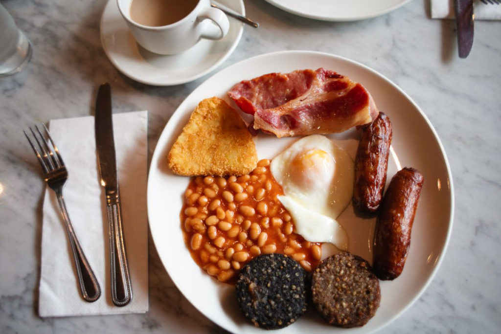 plate of Irish breakfast including bangers, sausage, eggs, potato hashbrown, and uncured bacon