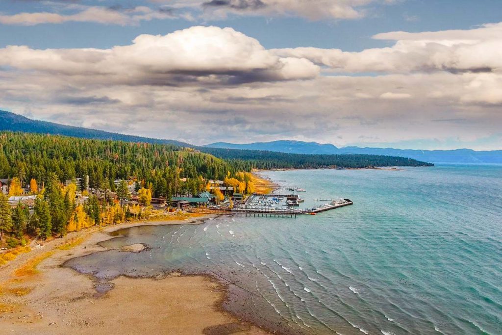 Lake Tahoe from atop a mountainside with turquoise waters and green and yellow trees on the mountains to the left and in the distance