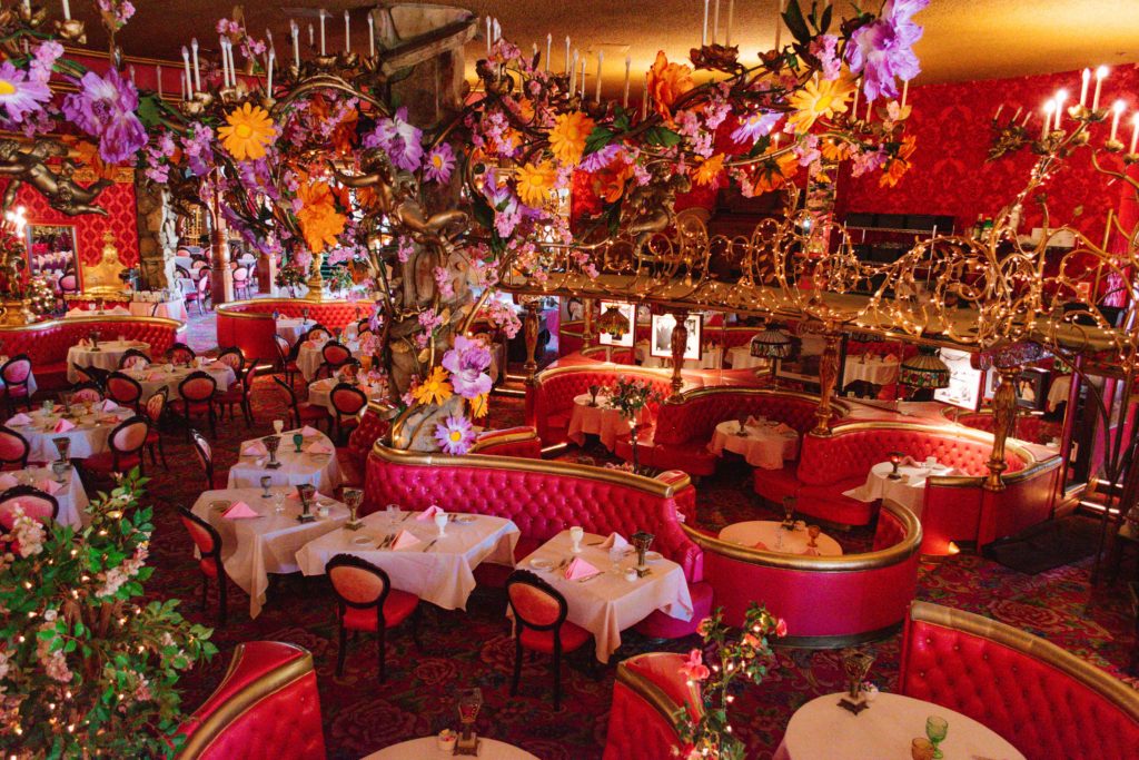 Interior of pink kitschy steak house with pink booths and chairs, a floral chandelier, and candles