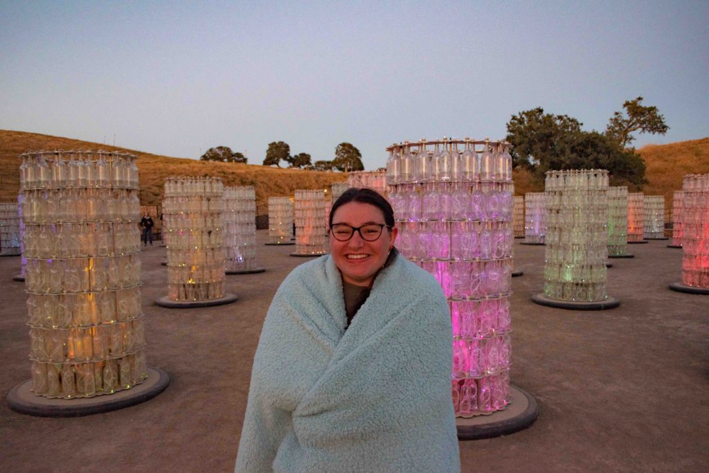 woman wrapped in a light blue blanket in front of a light tower exhibit outdoors