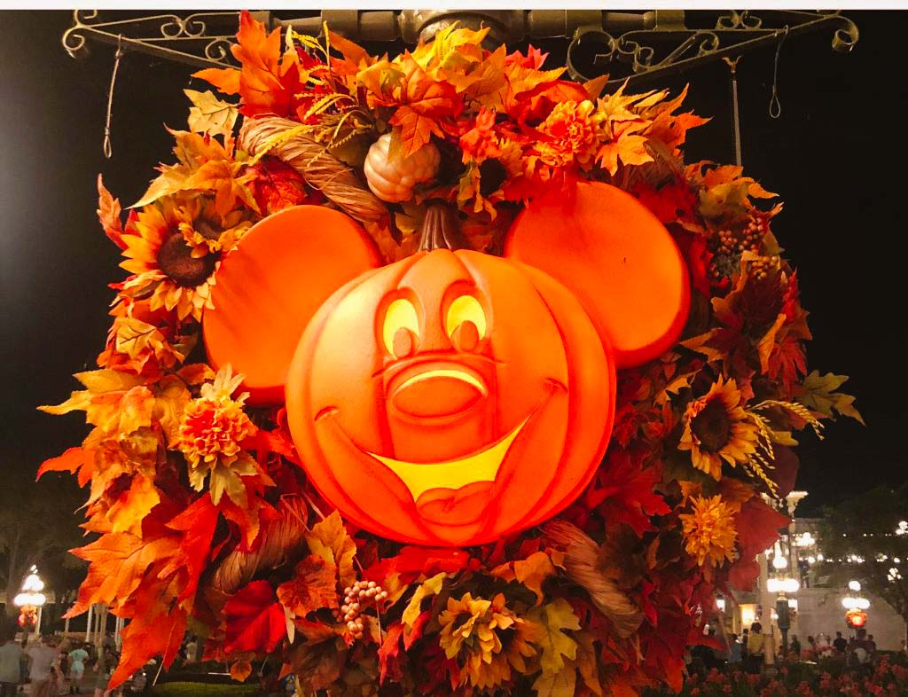 Mickey pumpkin with a fall wreath behind on a lamp post in Magic Kingdom in Orlando Florida