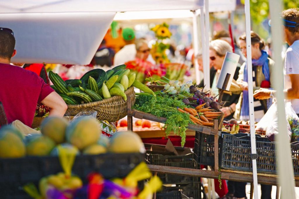 view from the side of a vendor's booth of a farmers market of booths of produce.