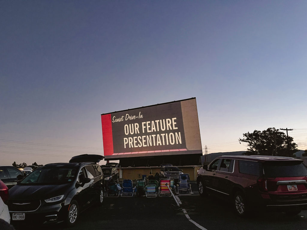 View of a drive in movie screen with cars in front.
