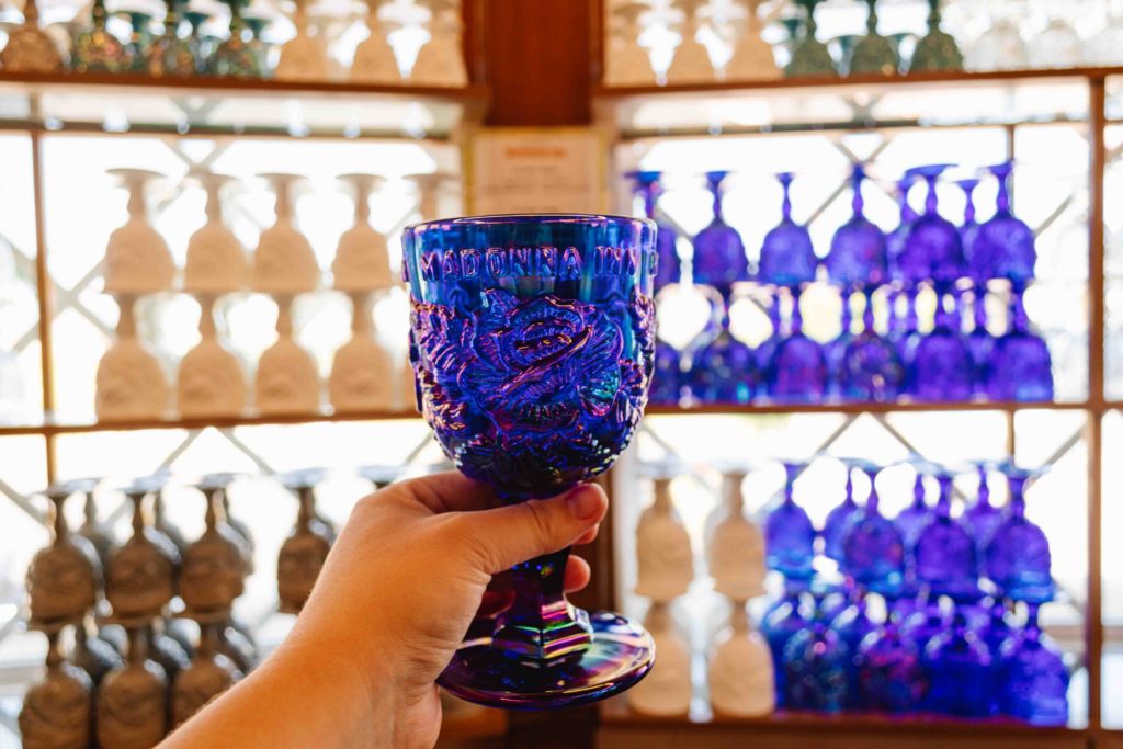 Madonna Inn goblets stacked against a window with a woman's outstretched hand holding a cobalt blue glass one