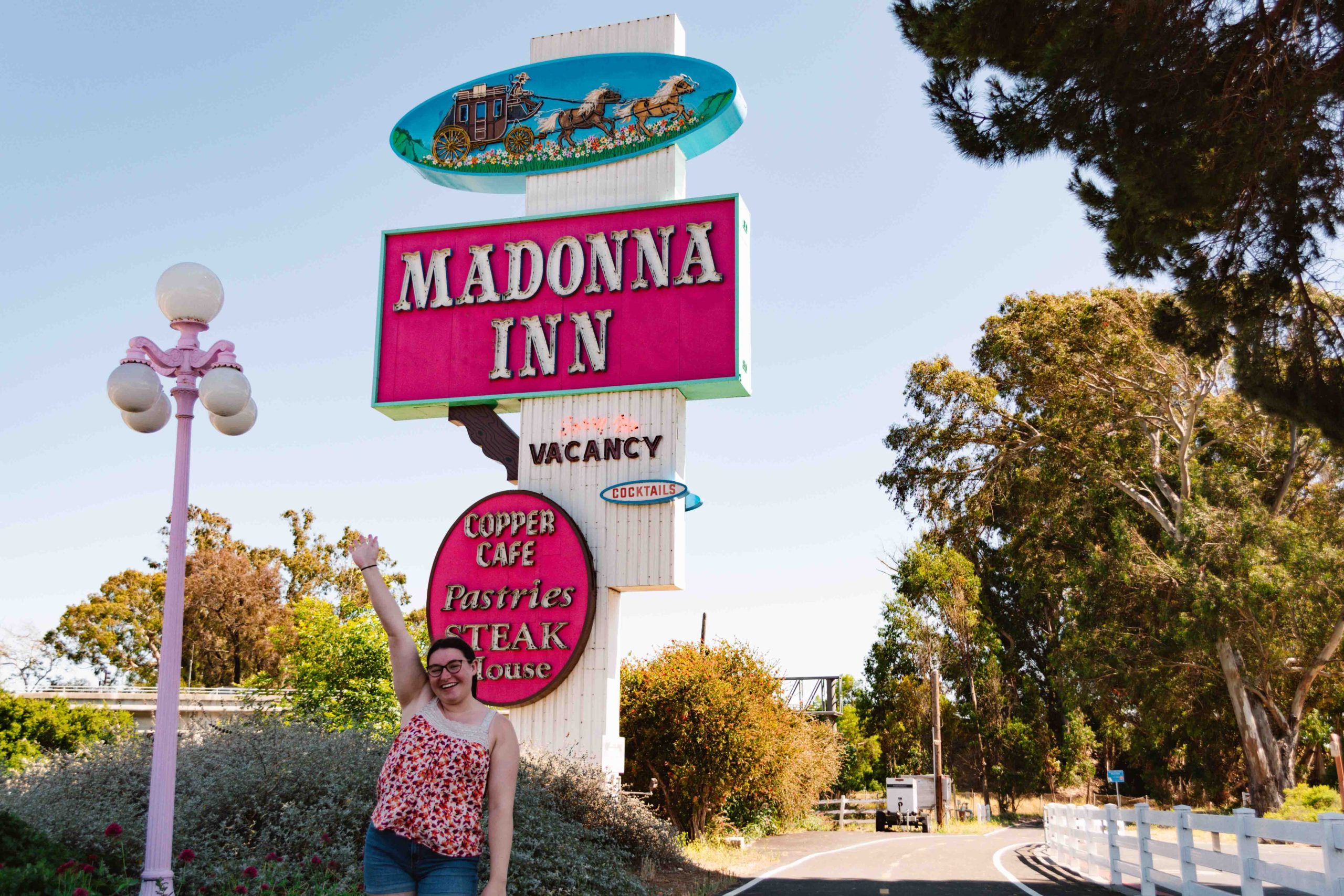 Woman taking a photo with a pink neon sign of Madonna Inn with stagecoach on the neon