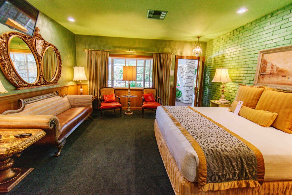 Green hotel room with red chairs, a leather couch, and over the top decor.