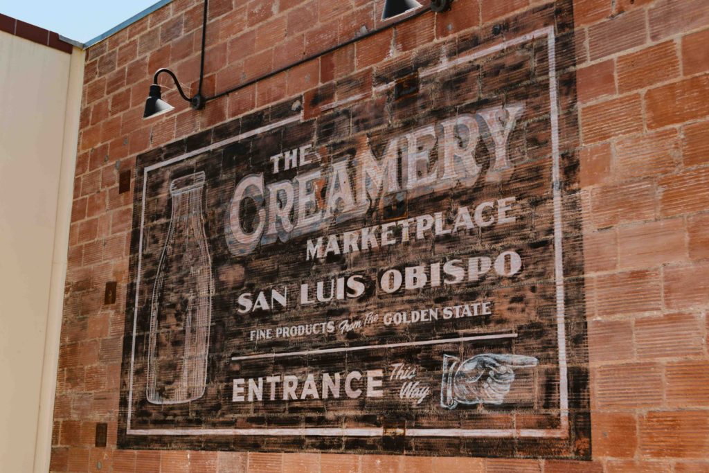 vintage painted sign on a brick wall that says The Creamery Marketplace San Luis Obispo Entrance
