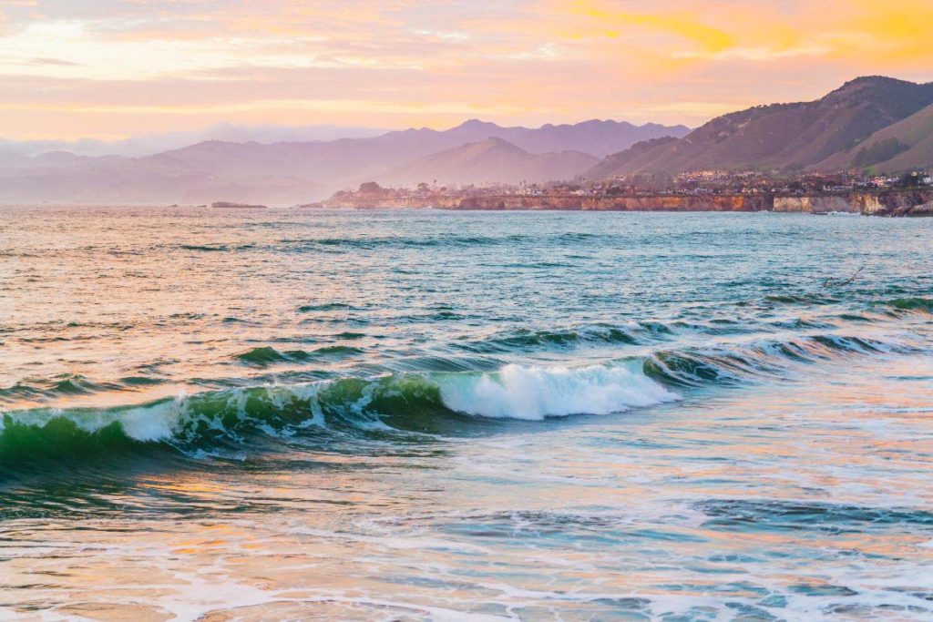 Pismo Beach in San Luis Obispo county during sunset with purple mountains, and an orange sky