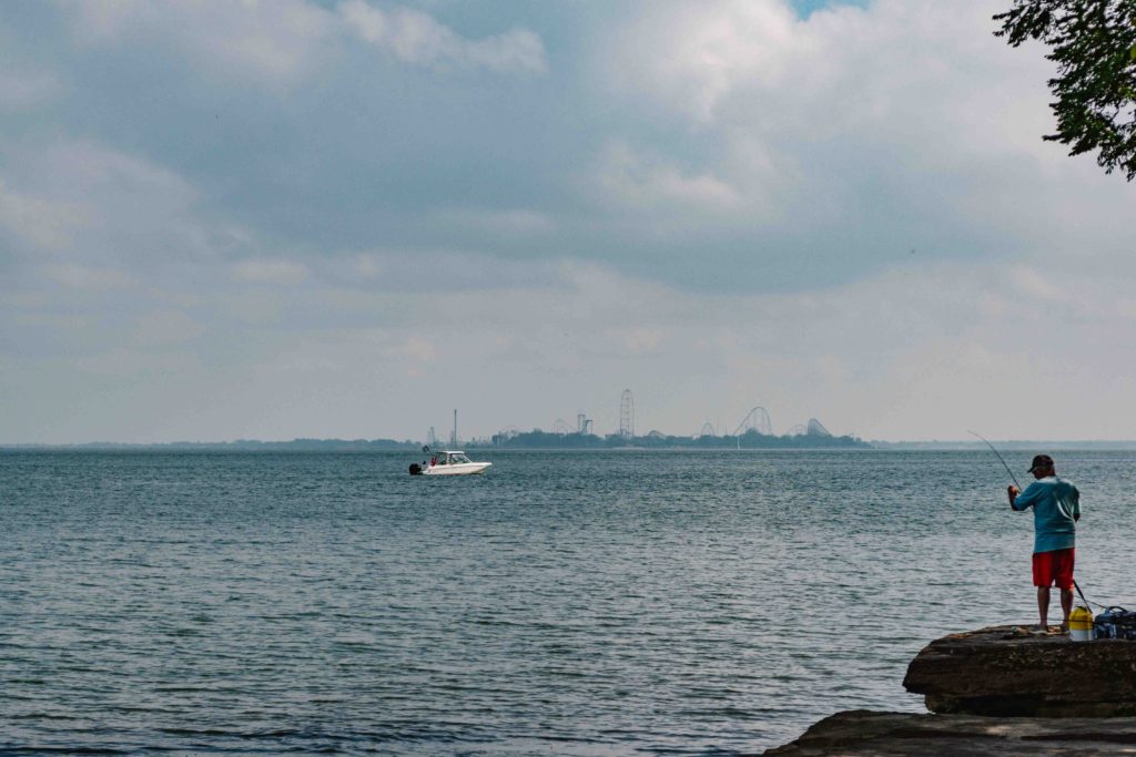 Ohio coast line showing Cedar Point theme park with boat on the water and fisherman in the foreground
