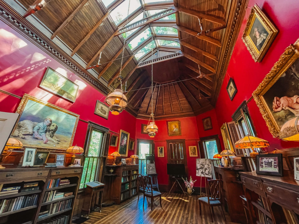 Historic Westwood home of Adelia Lutz, the artist, with her studio shown with red walls, paintings on the walls and a wooden vaulted ceiling with a sky light in the center