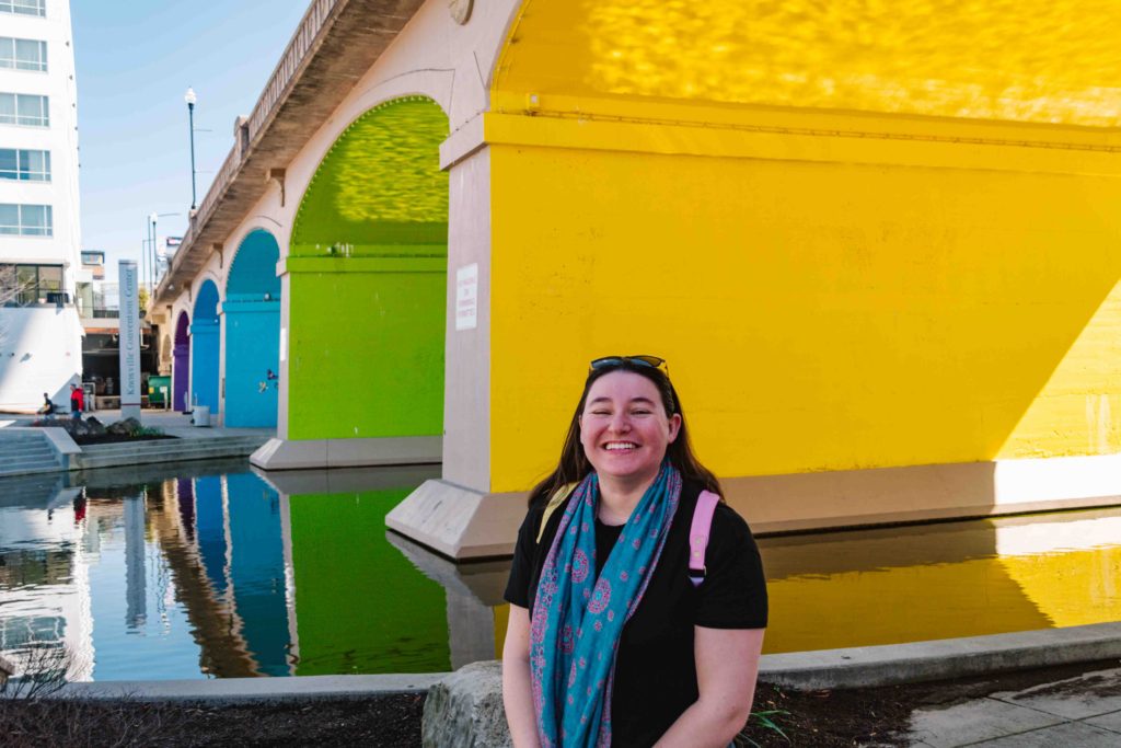 Rainbow arches in color sequence with a woman standing in front smiling.