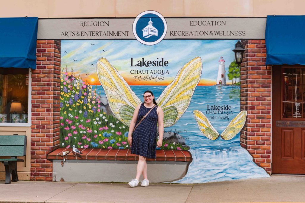 Woman in a blue dress posing with Lakeside Chautauqua mural of mayfly wings