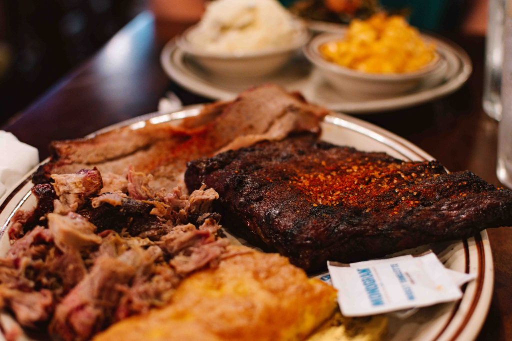 Barbeque sampler platter with pulled pork, ribs, and more piled high on the plate.