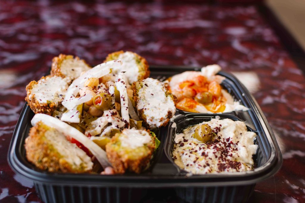 Six falafel halves with tahini on top and hummus and baba ganoush on the side to the right