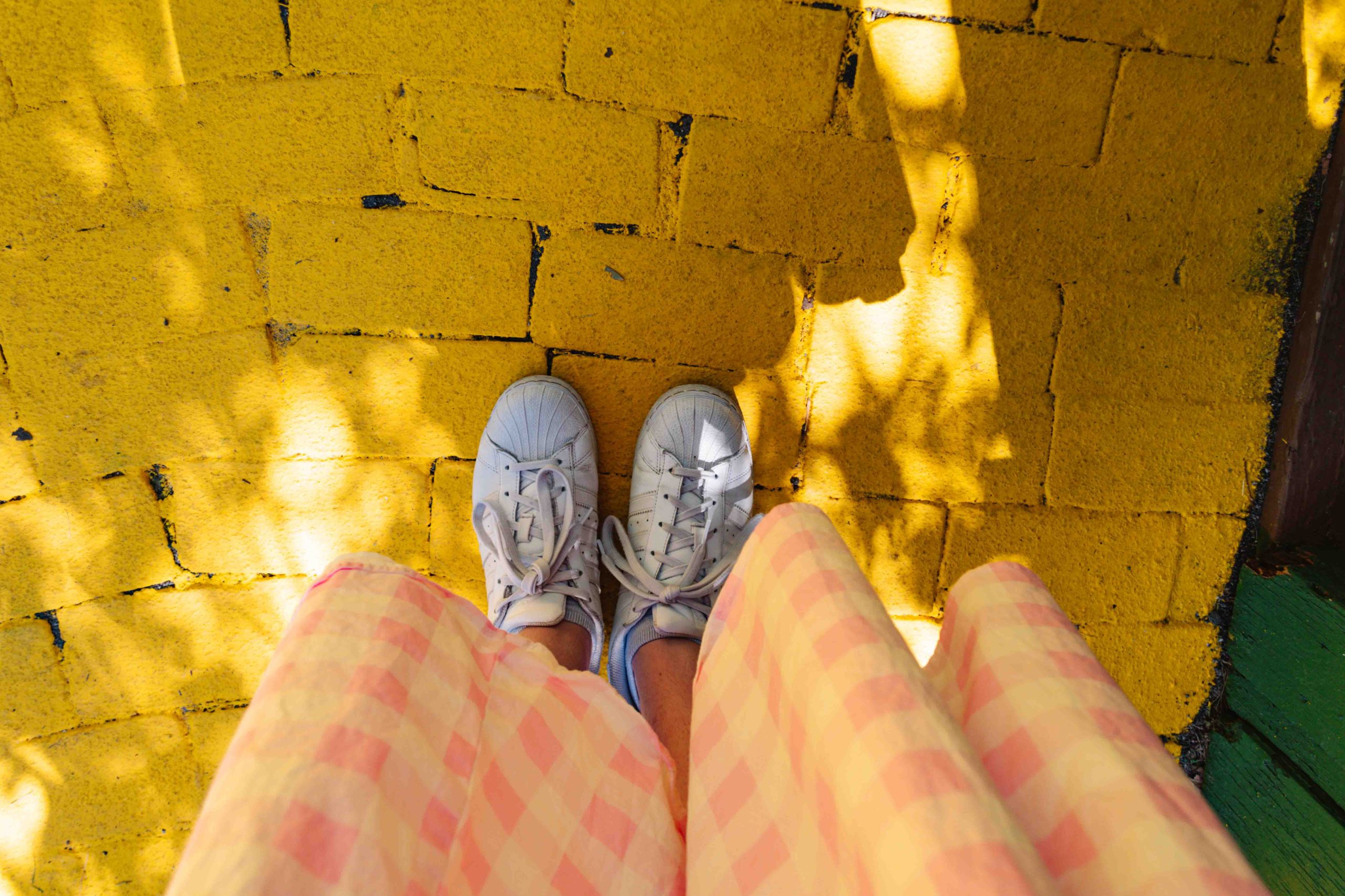 Woman in a pink gingham dress standing on yellow brick road view looking down at her feet