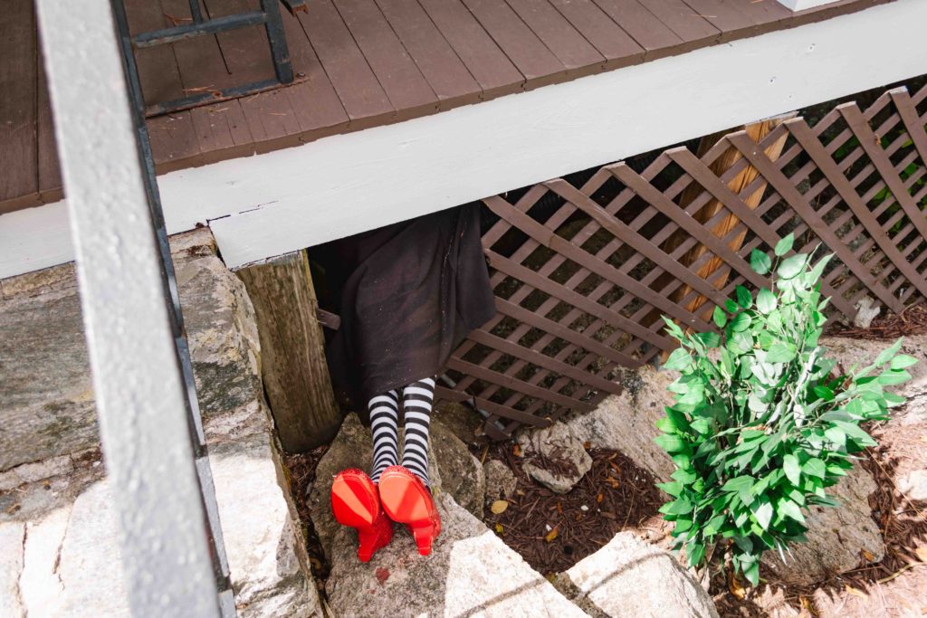 Wicked Witch of the East's black and white striped stocking covered legs sticking out from under Dorothy's house with her red slippers on.