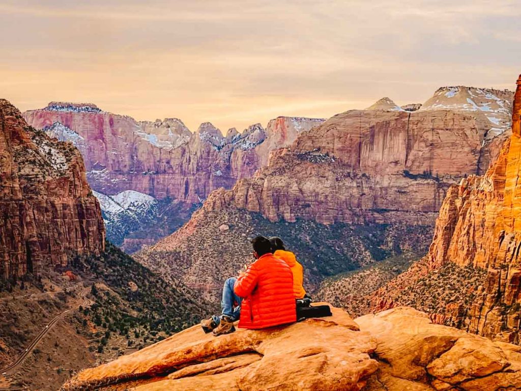 Zion National Park sunset in spring with a couple sitting on a mountain peak looking at the valley ahead