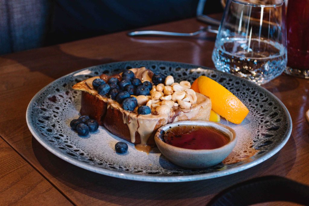 ceramic blue and white plate with peanut butter french toast on top with a side of syrup and topped with blueberries and peanuts