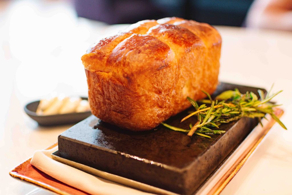 House bread loaf on a hot stone plate with oil and fresh herbs cooking on the tablet with it