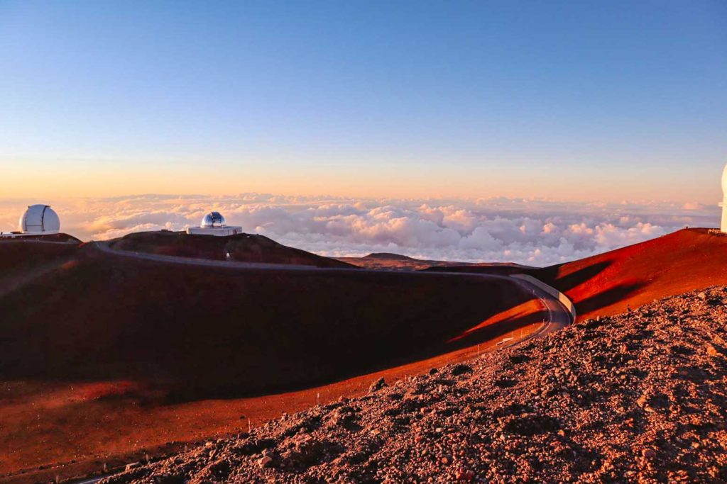 View of Maunakea Observatories from atop a mountain peak looking out above the clouds at sunrise or sunset, which makes for a wonderful spring destination and activity