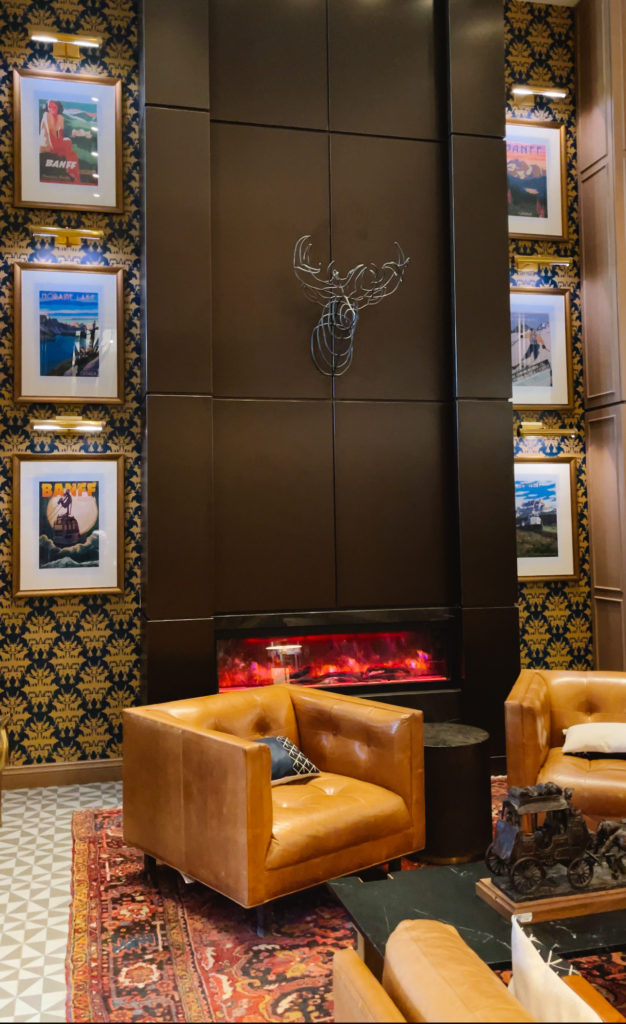 Cozy hotel lobby with electric fireplace, leather chairs, and historic vintage travel posters on the wall