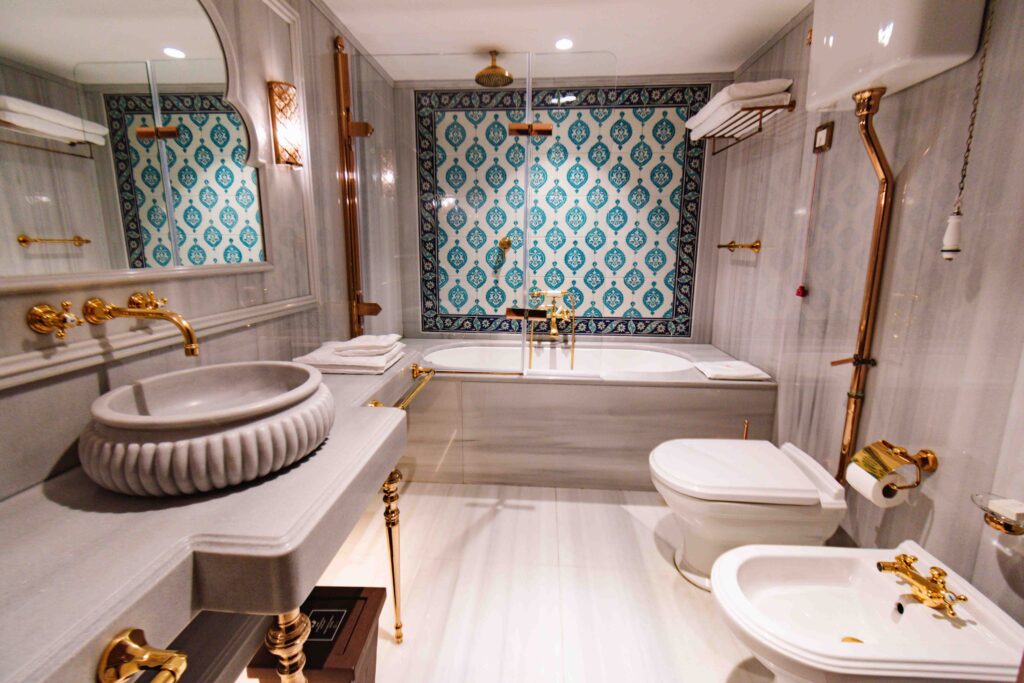 Interior view of Ottoman Empire style bathroom with ornate blue tiles on the wall by the bathtub and marble counters and sink