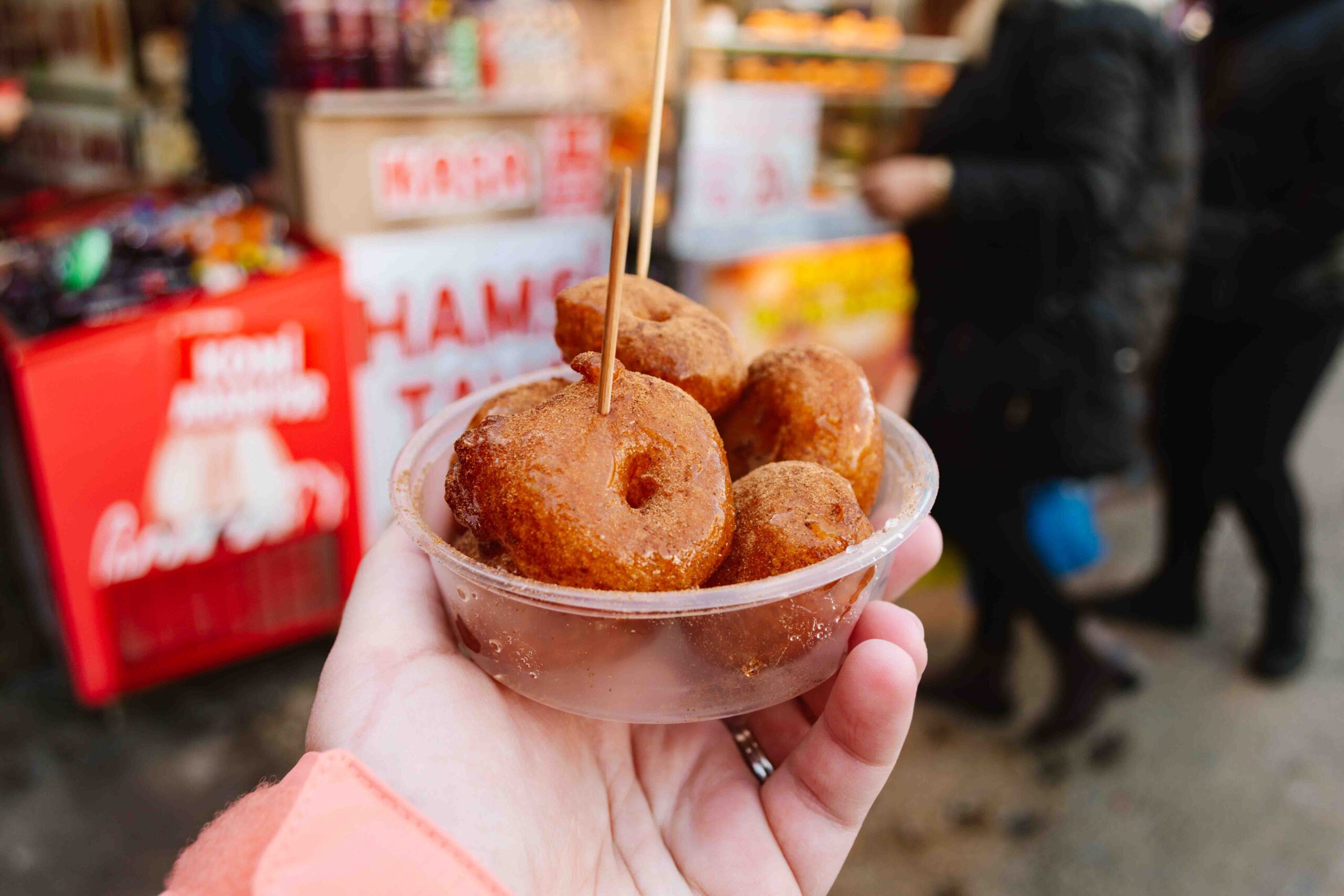 Woman holding a small clear plastic bowl of lokma, a Turkish street food that looks like cinnamon topped donuts -- one of the best things to eat on a food tour of Istanbul