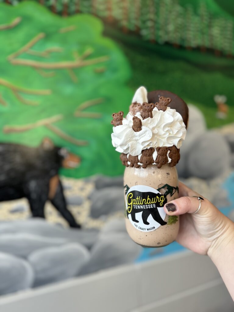 Woman's outstretched hand holding a crazy milkshake called Meet Me in the Mountains, specialty from Gatlinburg