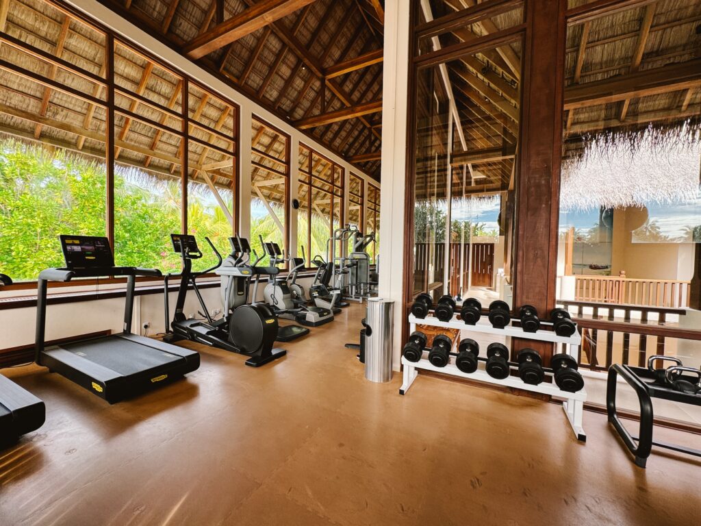 Gym at 5 star resort in Maldives including weightlifting equipment and cardio machines with tropical view