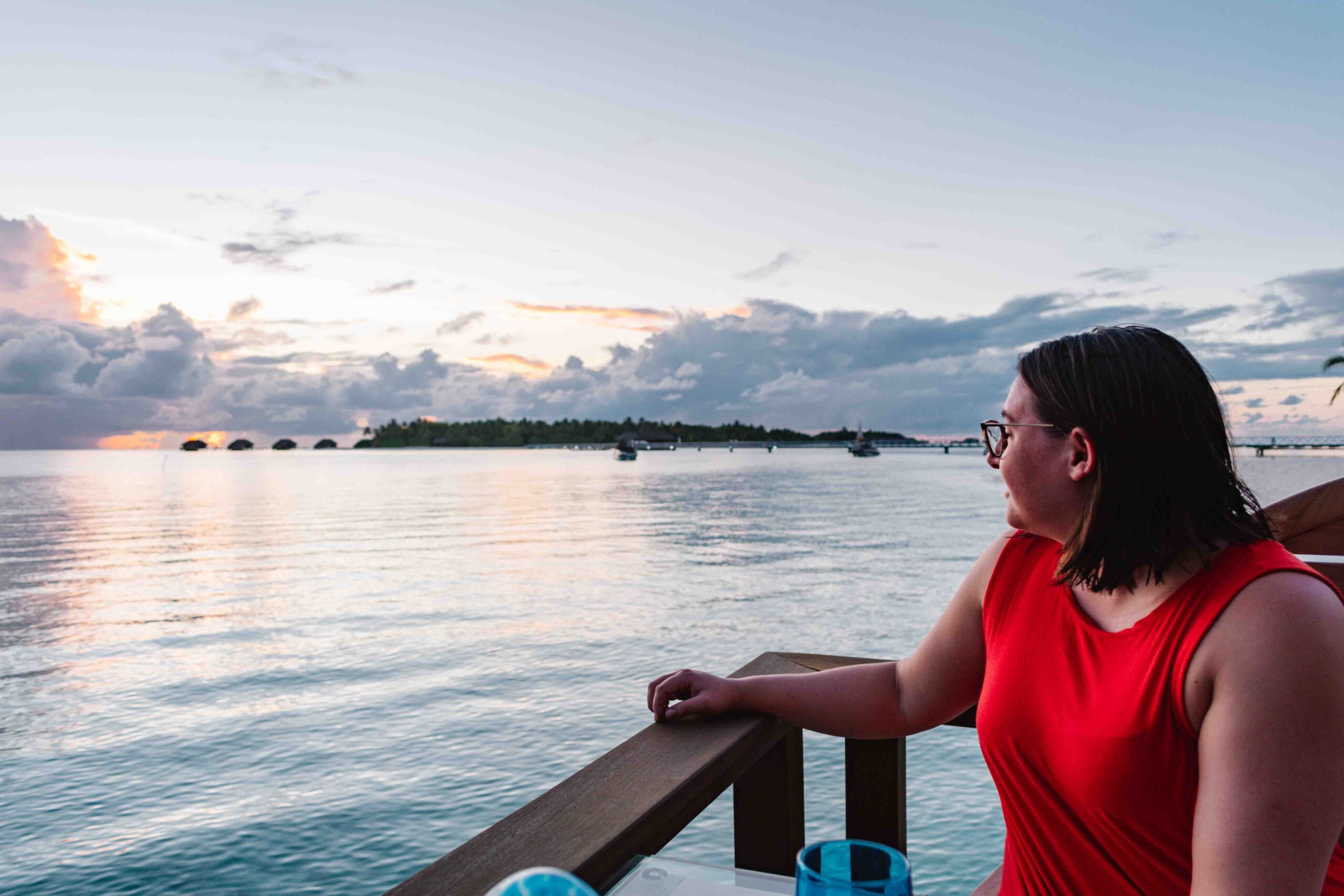Woman looking at the sunset from a restaurant table hovering over the water