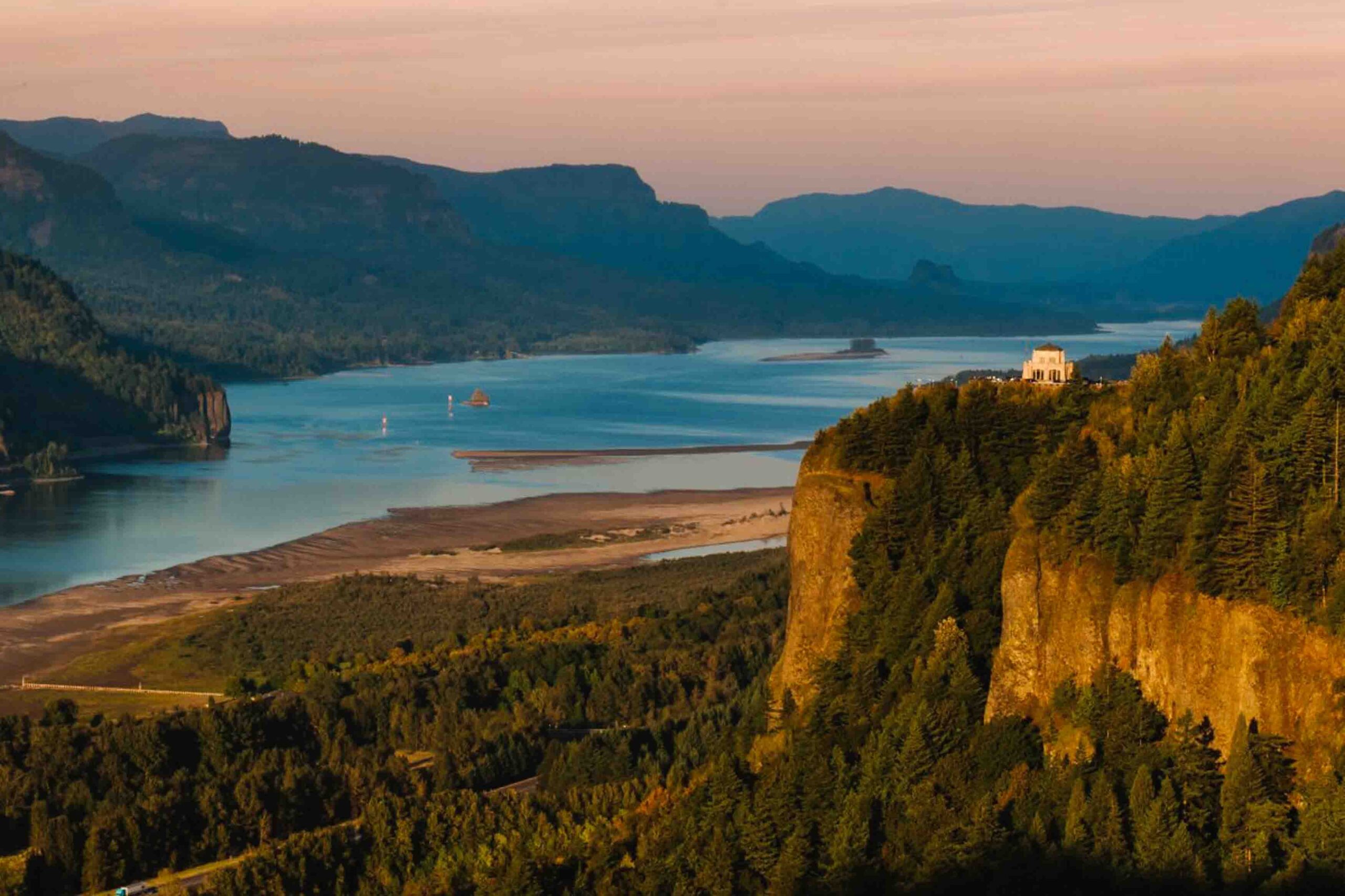 View of the Vista House along the Columbia River Gorge with the river and mountains in the background at sunset