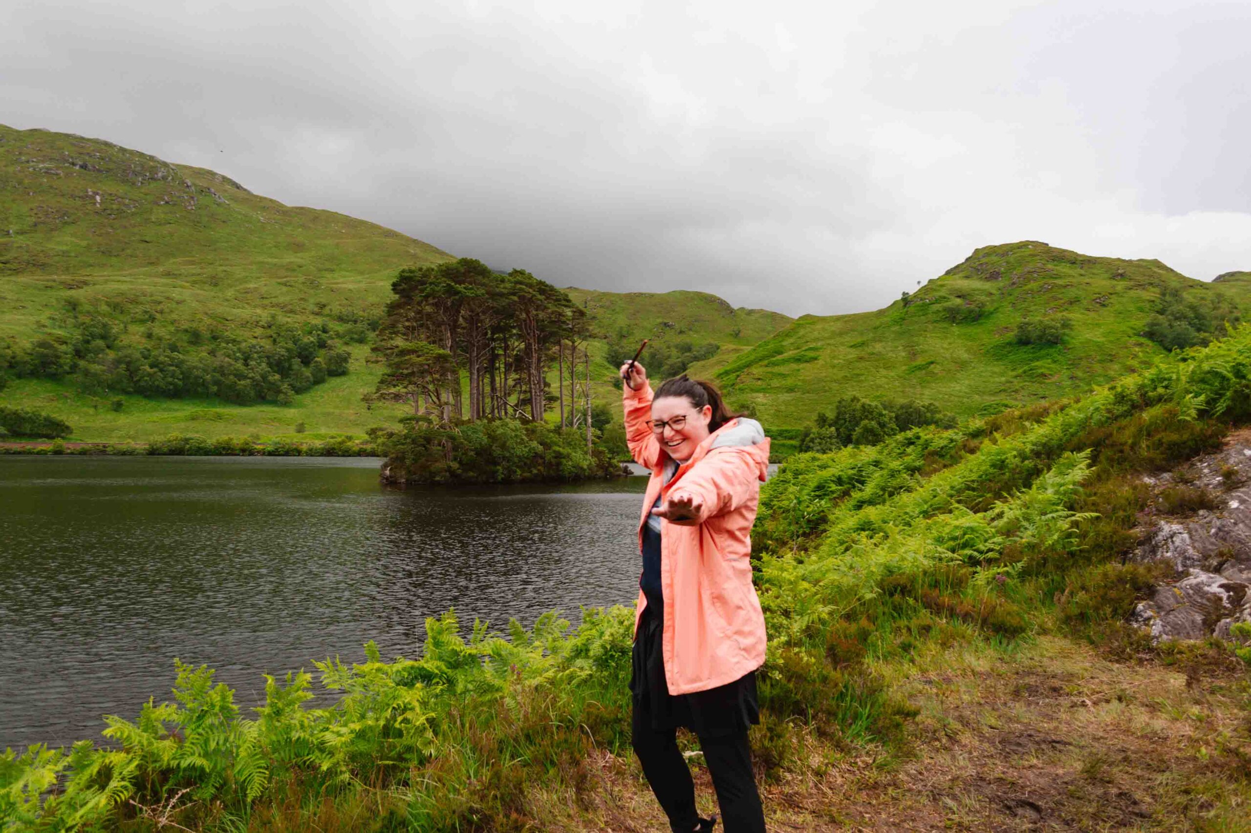 Woman pointing a wand at the camera in front of Dumbledore's burial site in Scotland