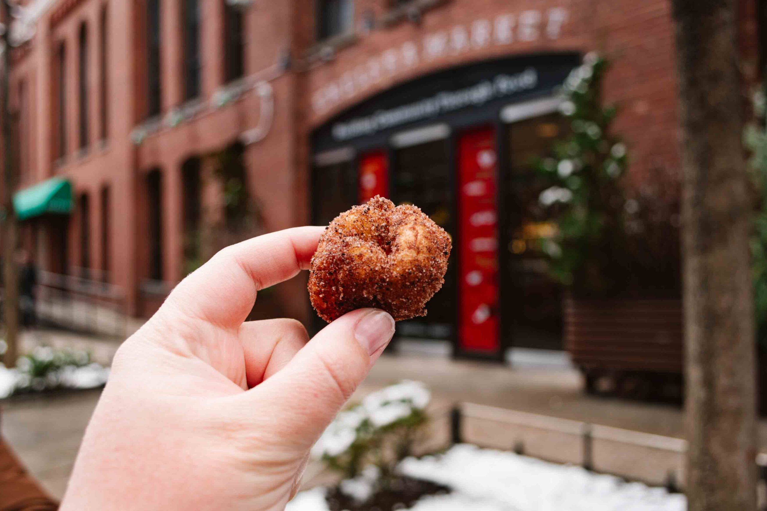 Woman's outstretched hand holding a mini donut covered in chocolate sugar sprinkles