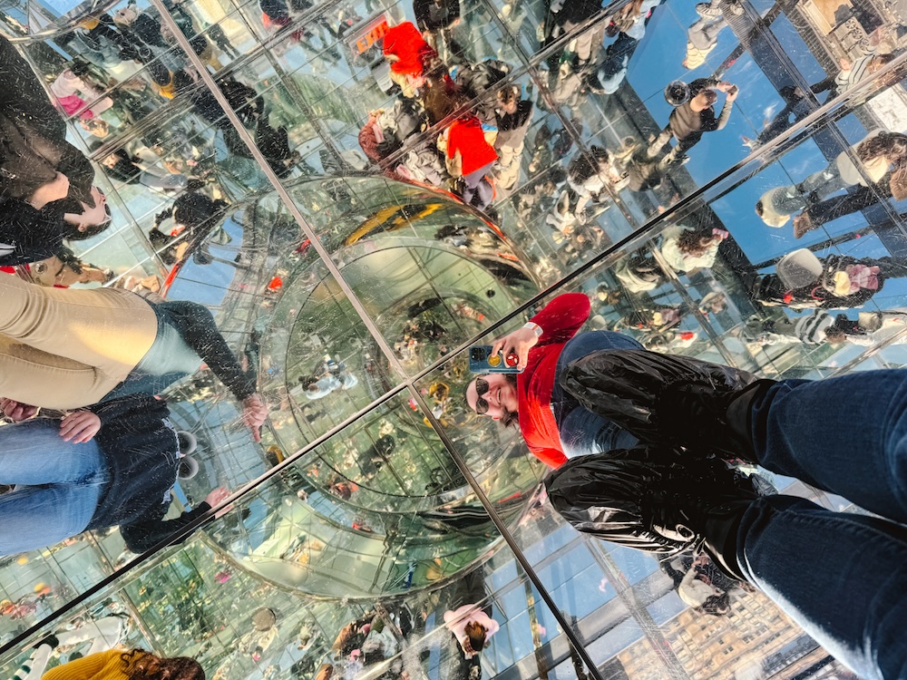 Woman looking into a mirrored floor thats reflecting all the other mirrors in the room as part of the art installation at Summit One in NYC