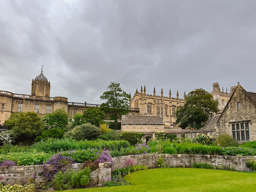 Exterior of Christ Church at Oxford during the summer with lots of purple flowers in bloom