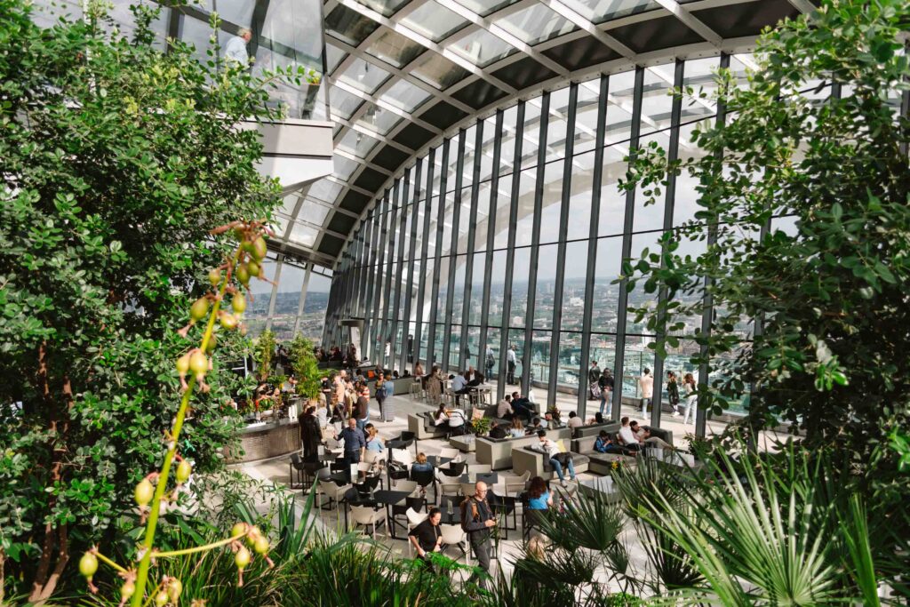 Interior view of Sky Garden from an upper floor peering through the plants at the seating below and large multi-story window ahead