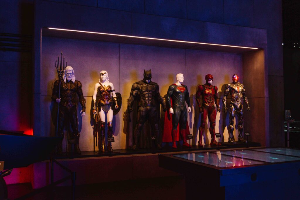 DC heroes costumes on display including Wonder Woman, Superman, Batman, Aquaman, and the Flash