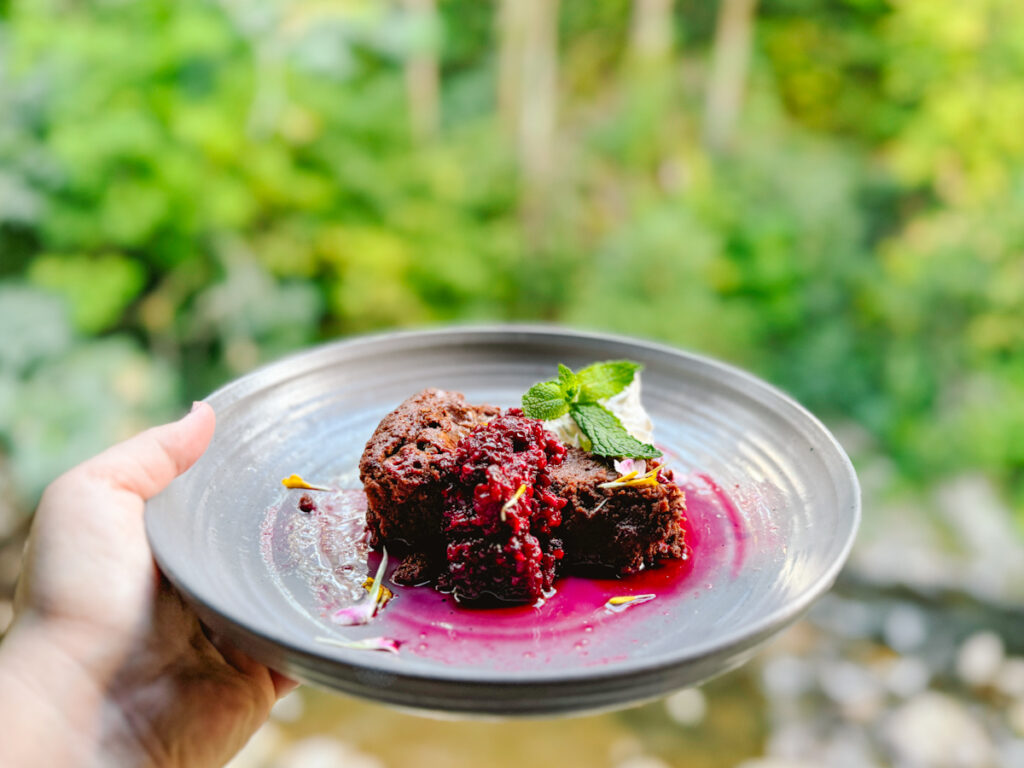 Woman's outstretched hand holding a chocolate tart with raspberries on top