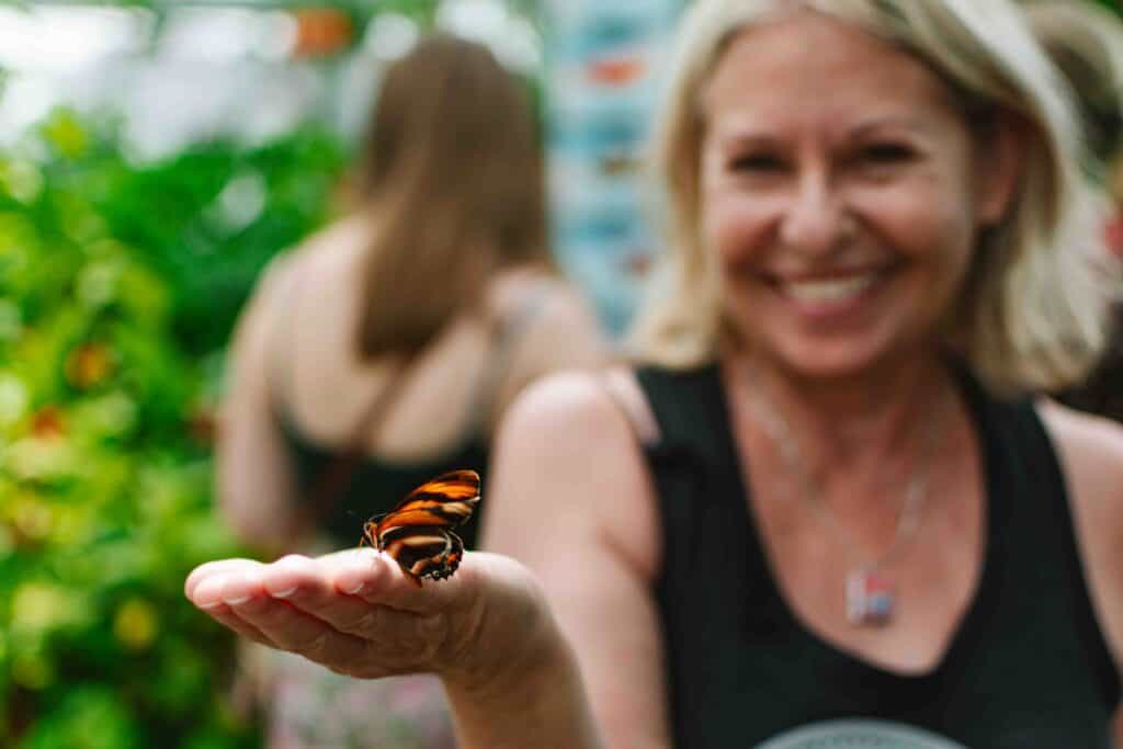 Woman holding a butterfly on her hand inside an aquarium exhibit