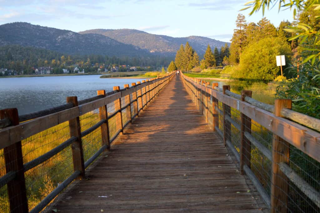 Lake side boardwalk during sunset in Big Bear California with mountains to the left background and greenery to the right