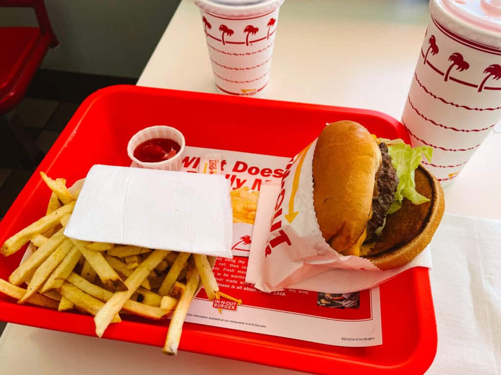 In-n-Out Burger meal of a cheese burger and fries on a red tray with two drinks in the background, an iconic stop on a SoCal road trip itinerary
