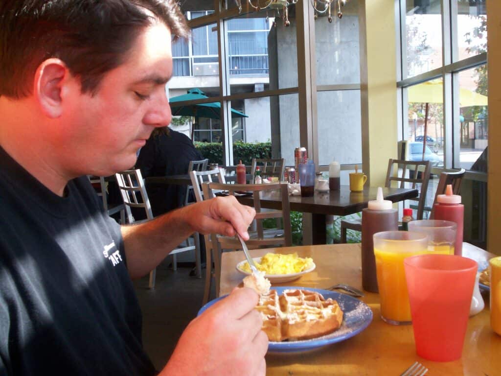 Man eating a waffle at a small cafe dressed in a black shirt