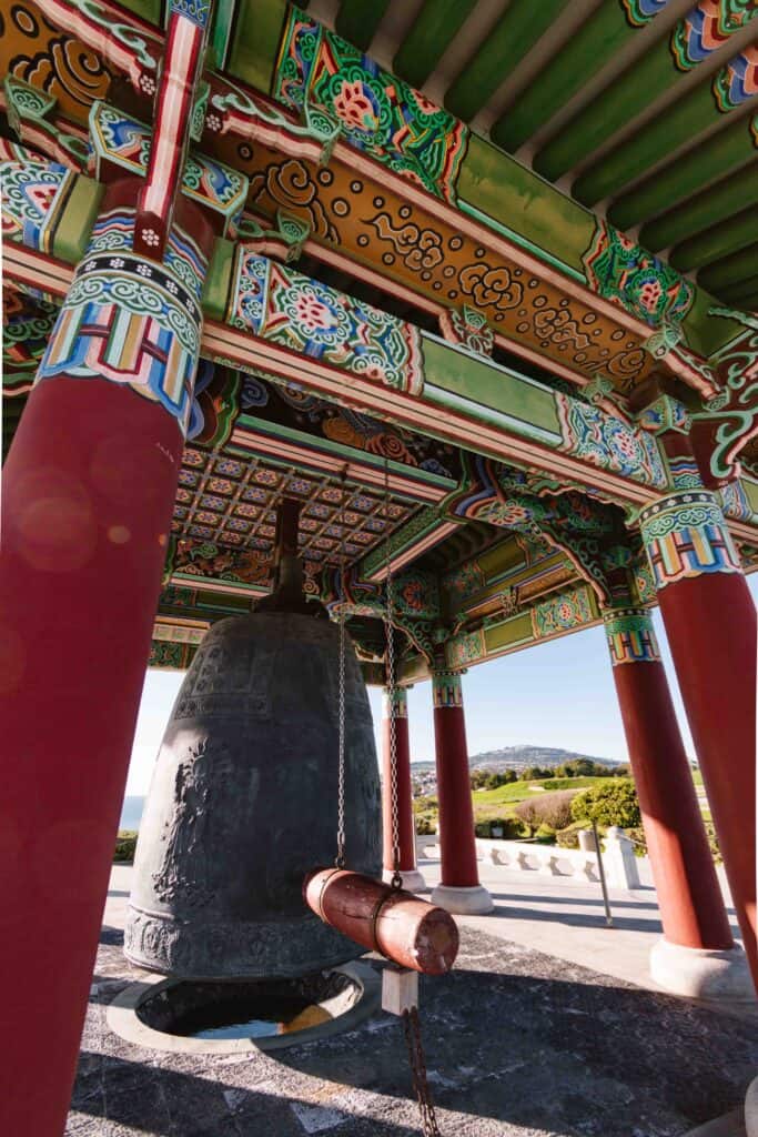 Vertical wide angle view of the Korean Friendship Bell in Los Angeles with red pillars and intricate green and pink roof