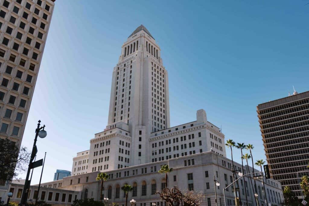 View of LA City Hall building from the ground looking up at the white tower building on a clear sunny day, where the Observation Deck at the top makes for a great free activity in Downtown LA