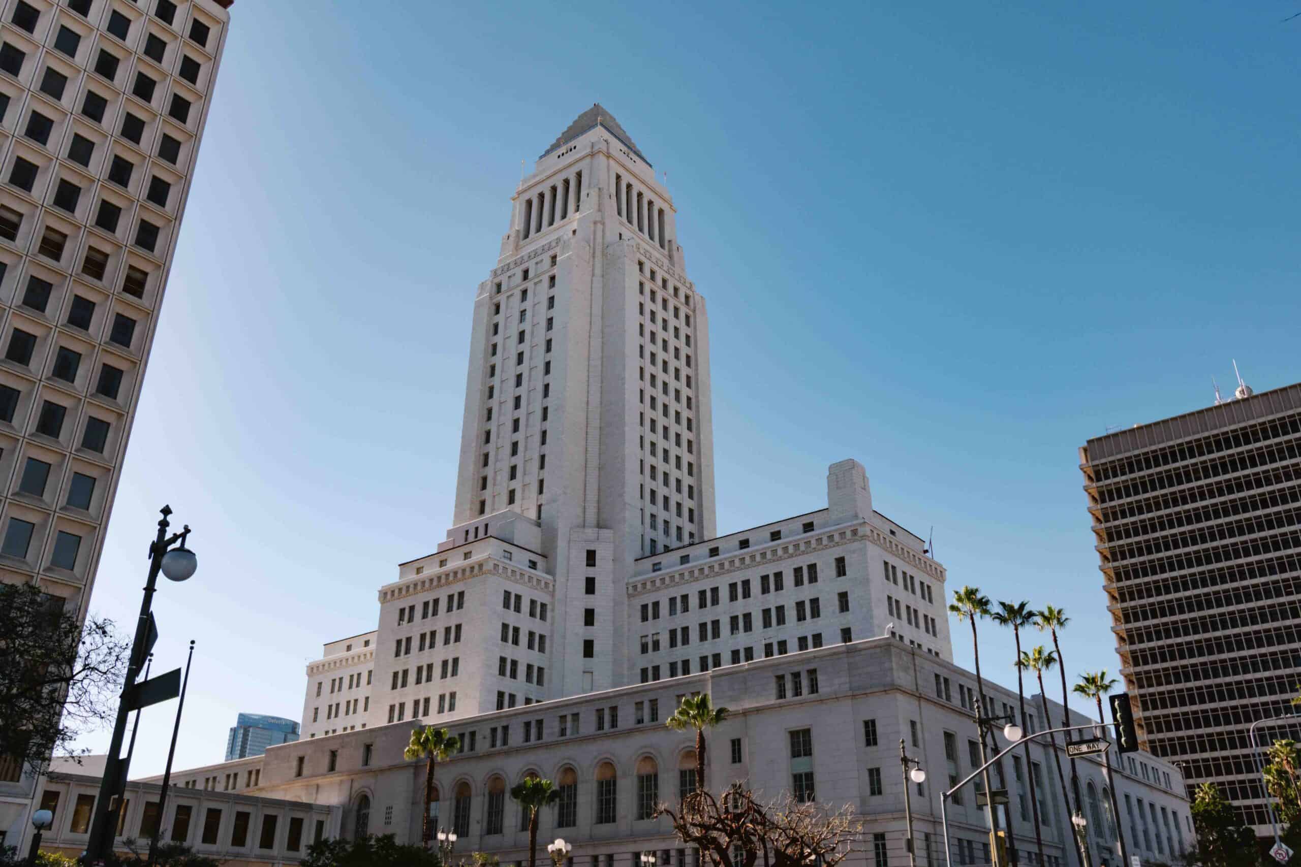 View of LA City Hall building from the ground looking up at the white tower building on a clear sunny day, where the Observation Deck at the top makes for a great free activity in Downtown LA