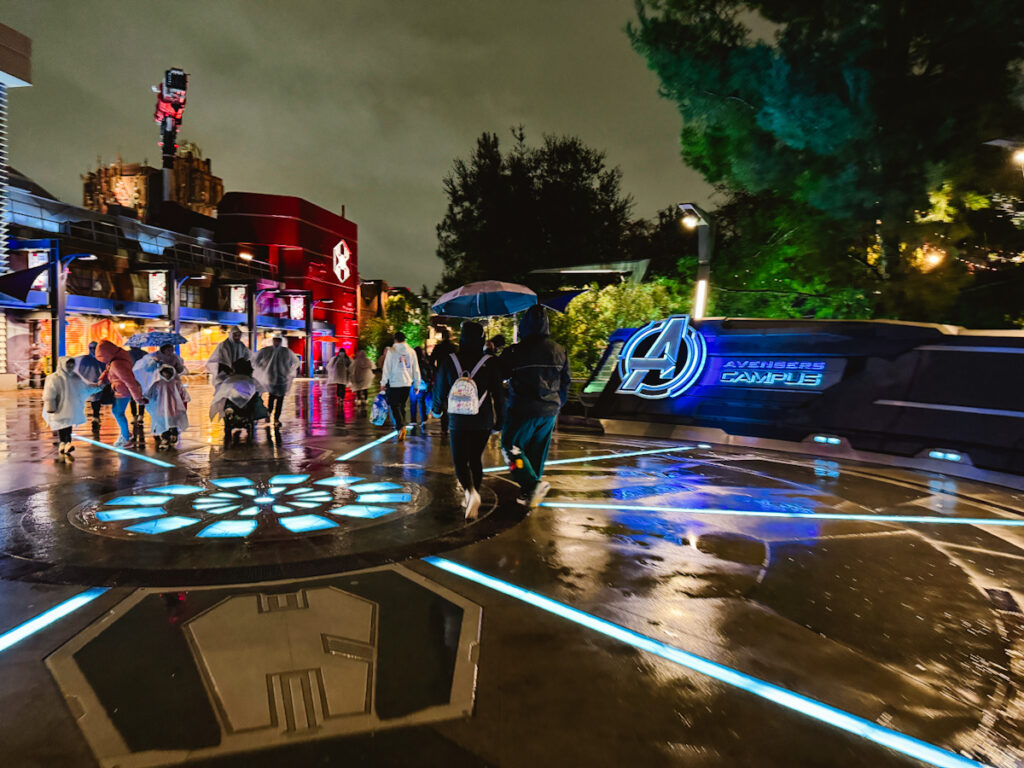 People walking in ponchos and with umbrellas through Avengers Campus in California Adventure theme park at night